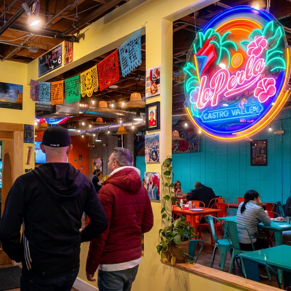 Colorful La Perla restaurant interior features a neon sign, Mexican papel picado decorations, and diners seated at bright tables.