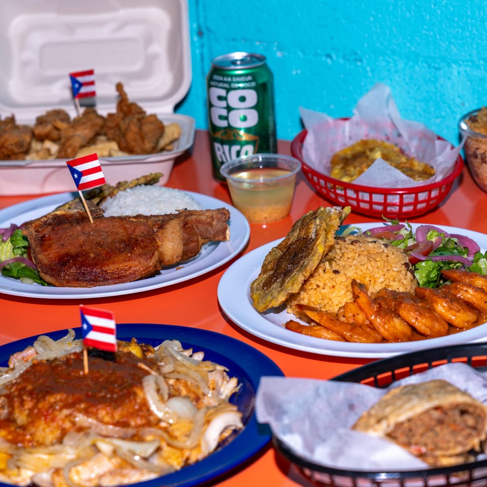 Assortment of Puerto Rican dishes, including roasted meats, rice, plantains, fried appetizers, and a can of coconut soda.
