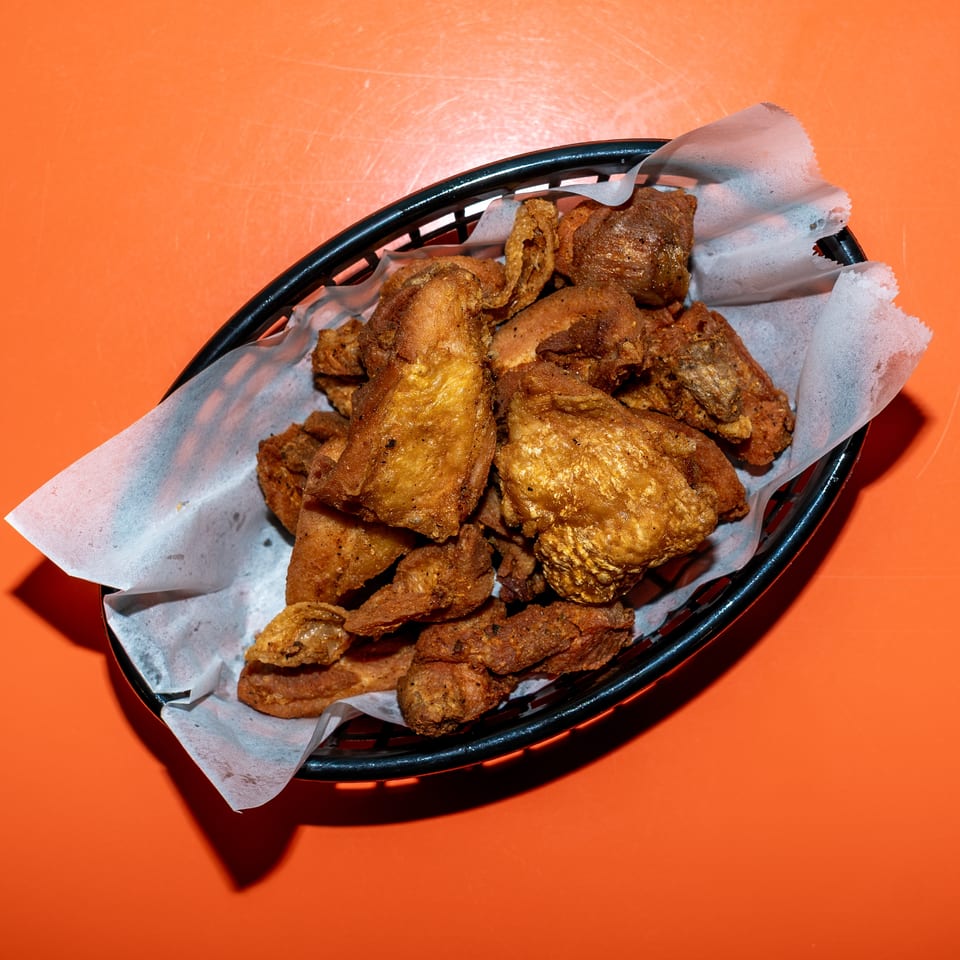 Basket of assorted golden-brown fried chicken pieces lined with paper on an orange tabletop.
