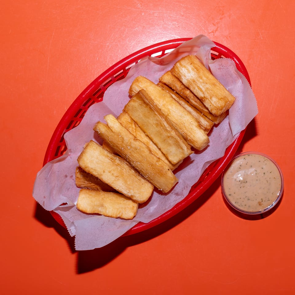 Golden fried sticks in a red basket with creamy herb dipping sauce on an orange tabletop.
