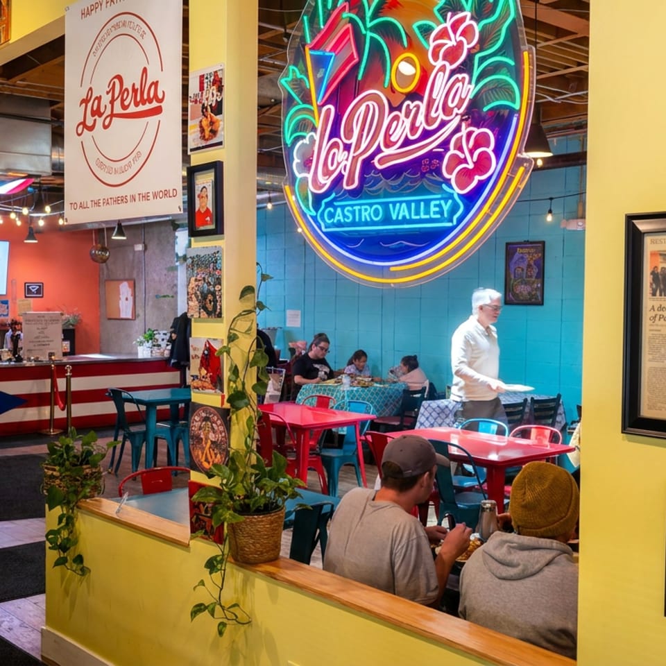 Colorful La Perla Puerto Rican restaurant interior with neon signage, red tables, diners, plants, and Puerto Rican décor.