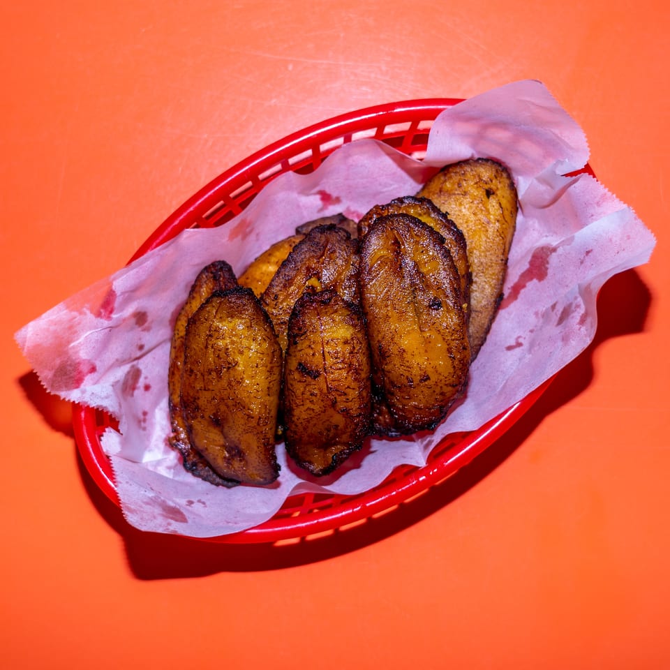 Grilled golden-brown pastries served in a red basket lined with paper on an orange table.