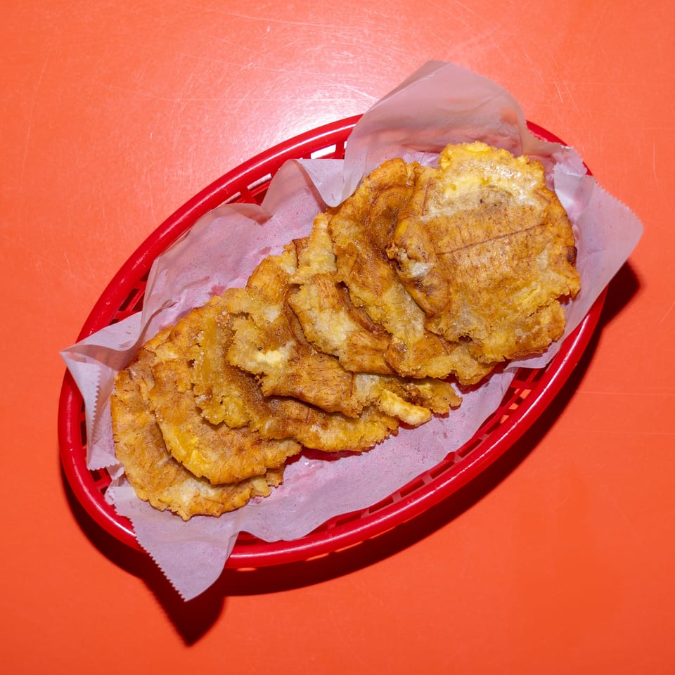 Basket of golden fried plantain slices lined with paper on a bright orange tabletop.