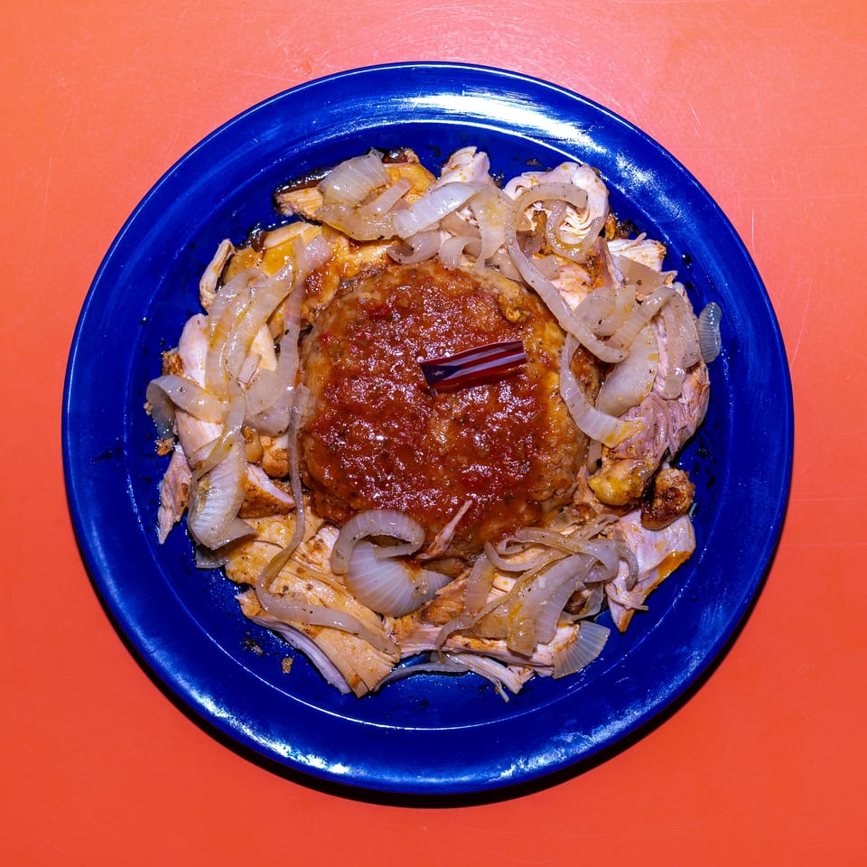 Blue plate holding saucy roasted chicken with sautéed onions and a small Puerto Rican flag garnish on an orange table.