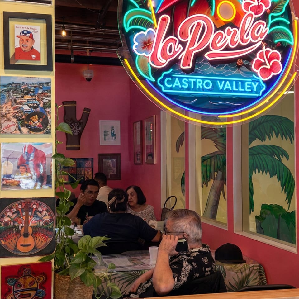 Colorful Castro Valley restaurant interior with neon La Perla sign, tropical murals, framed artwork, and diners seated at tables.